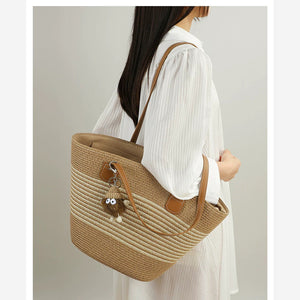Model carrying VINEY striped woven straw tote with plush charm, side view