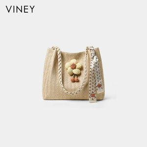 Beige woven summer tote with braided handles, flower charm and printed scarf, front view