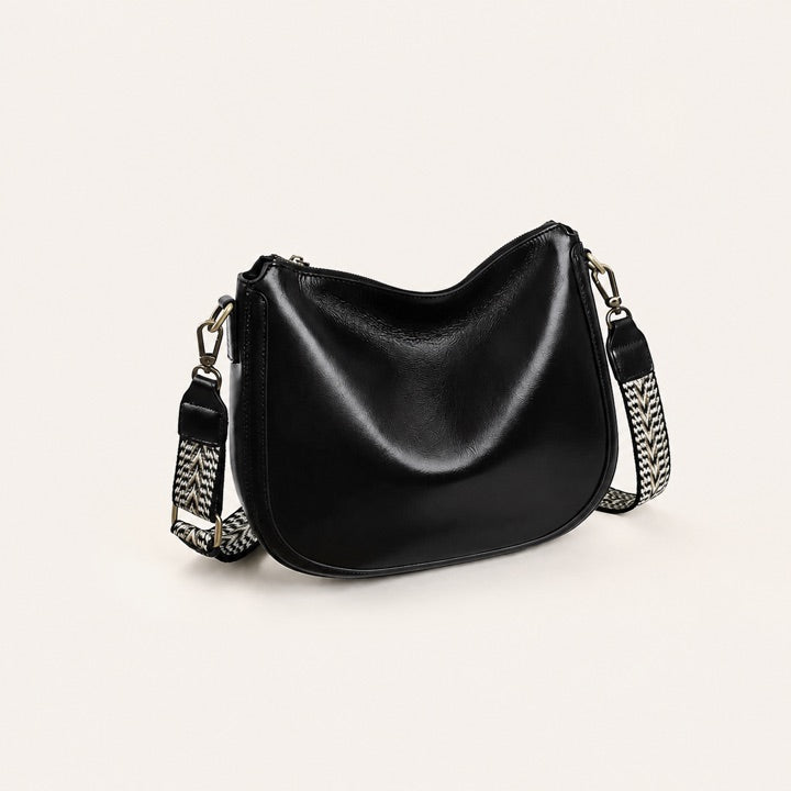 Black genuine leather saddle bag on a warm neutral studio background